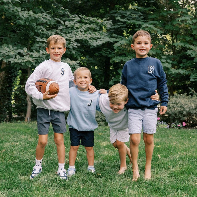 Children standing on grass wearing lettered sweatshirts
