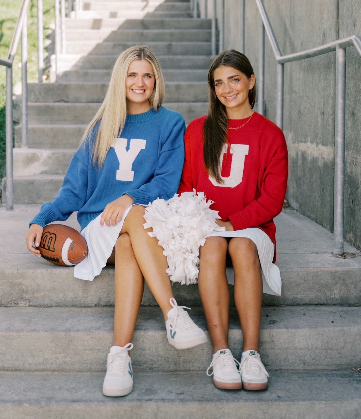 Two women wearing sweatshirts smiling while sitting on stairs