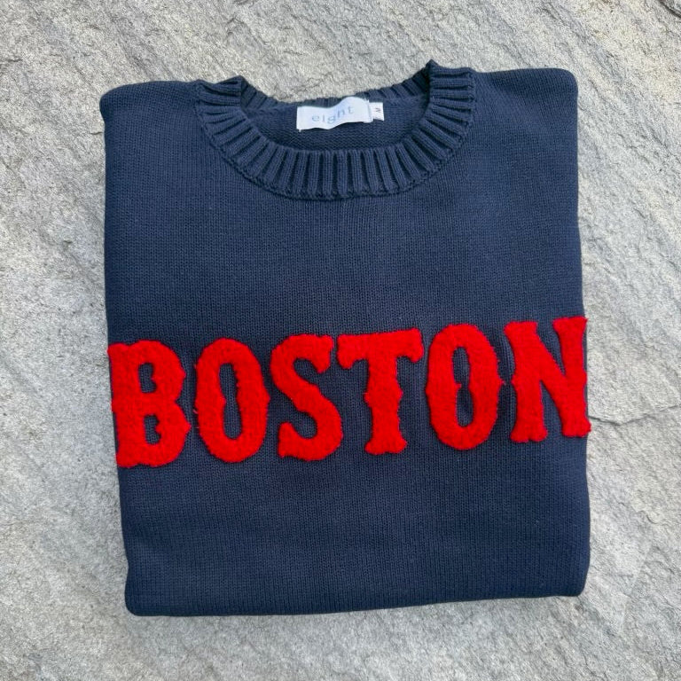 Folded navy blue sweater with 'BOSTON' in red on a textured surface