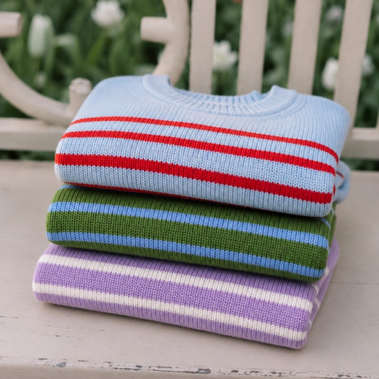 Stack of colorful striped sweaters on a wooden chair outdoors.