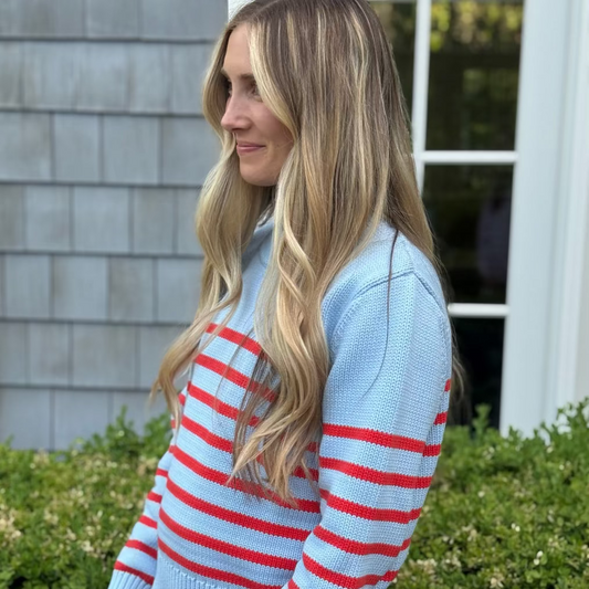 Woman wearing a light blue sweater with red stripes outdoors.