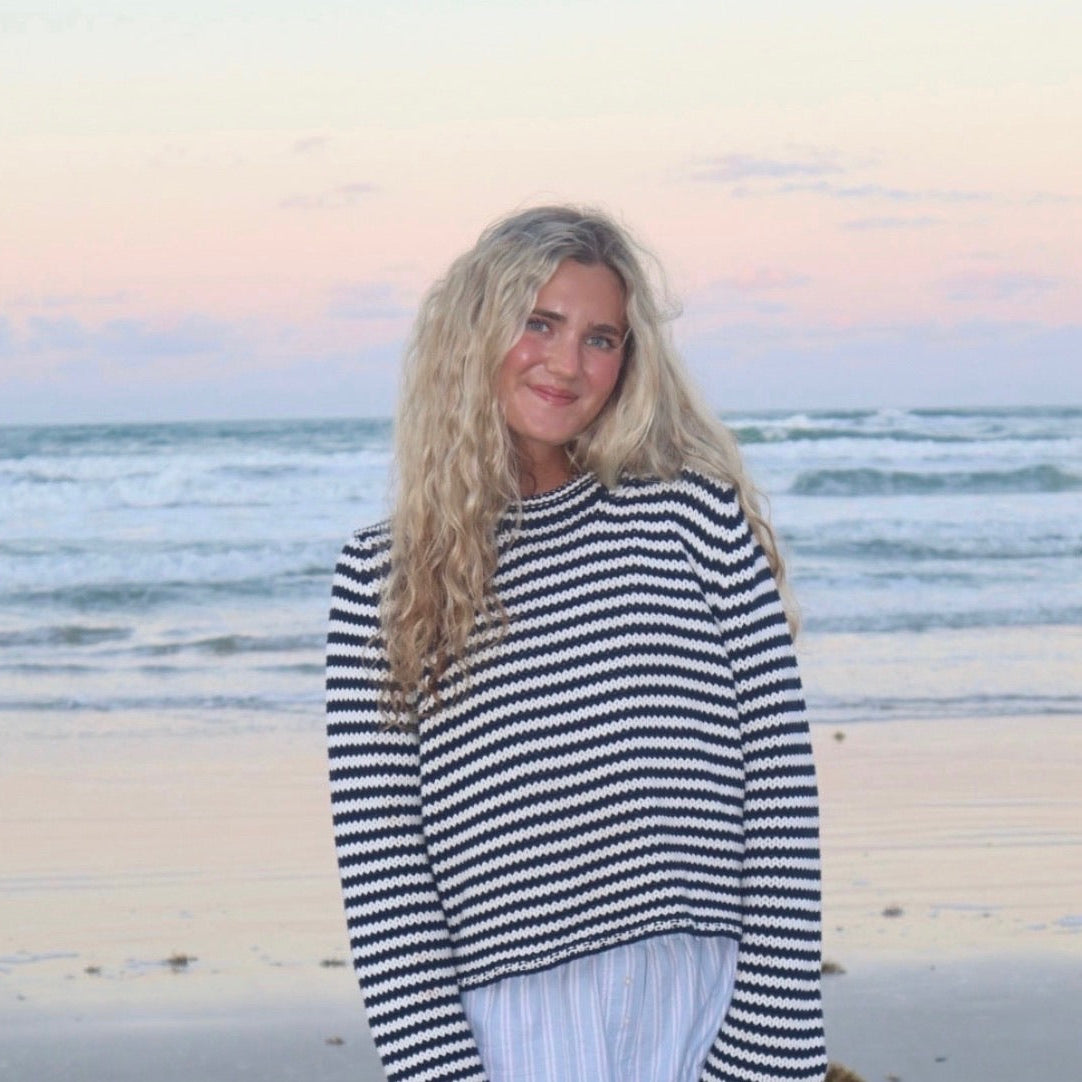 Woman in a striped sweater standing on a beach with ocean waves in the background