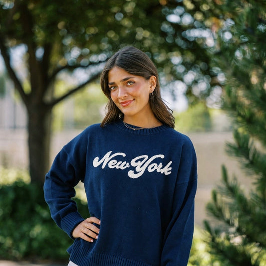 Woman wearing a navy blue sweater with 'New York' text, standing outdoors.