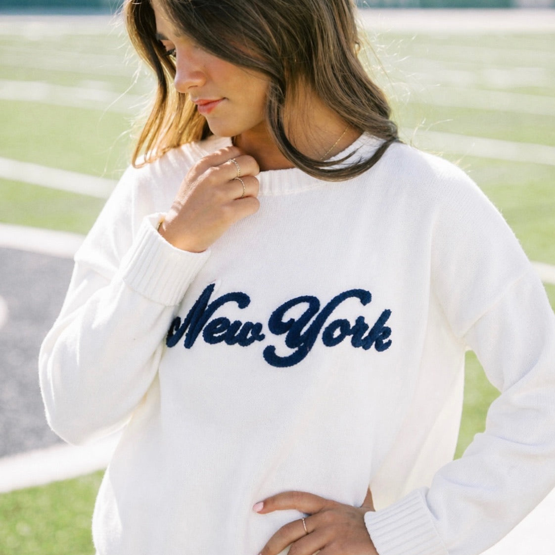 Woman wearing a white sweatshirt with 'New York' text outdoors.