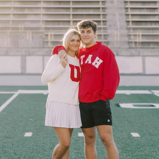 Two people posing on a football field with bleachers in the background