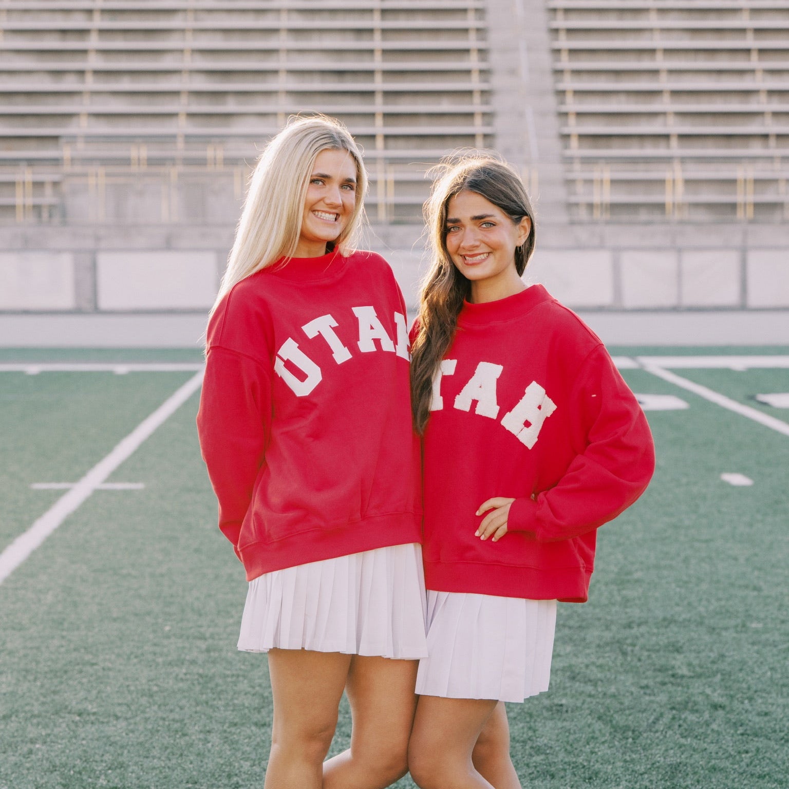 Two women wearing red sweatshirts with 'UTAH' text, standing on a sports field.