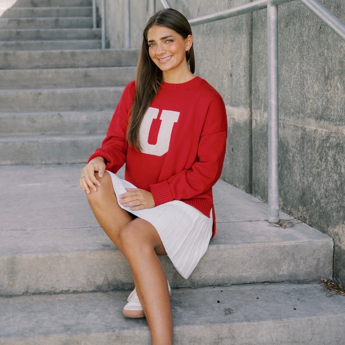 Woman in a red sweater with a large 'U' sitting on concrete steps.