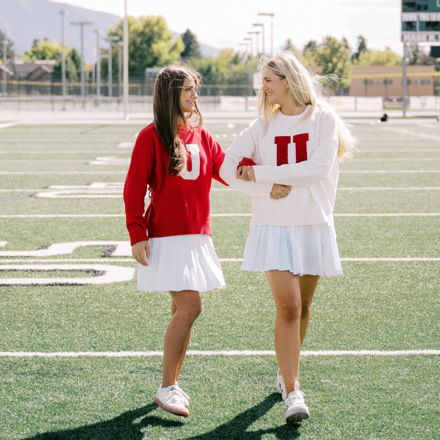 Two women in matching red and white sweaters on a football field