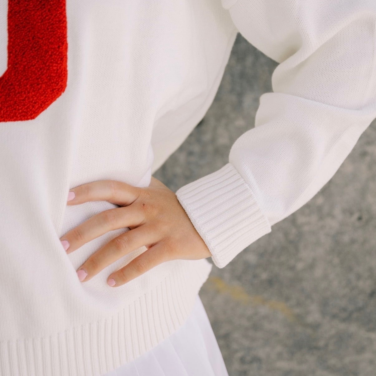 Close-up of a person wearing a white sweater with a red logo, holding their hand in front.