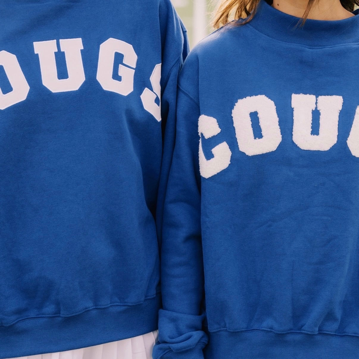 Two blue sweatshirts with 'COUGS' printed on them, worn by people.