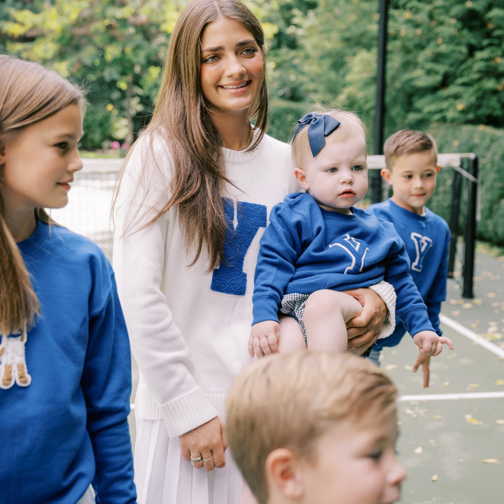 Woman holding a baby surrounded by children wearing blue shirts with a logo.