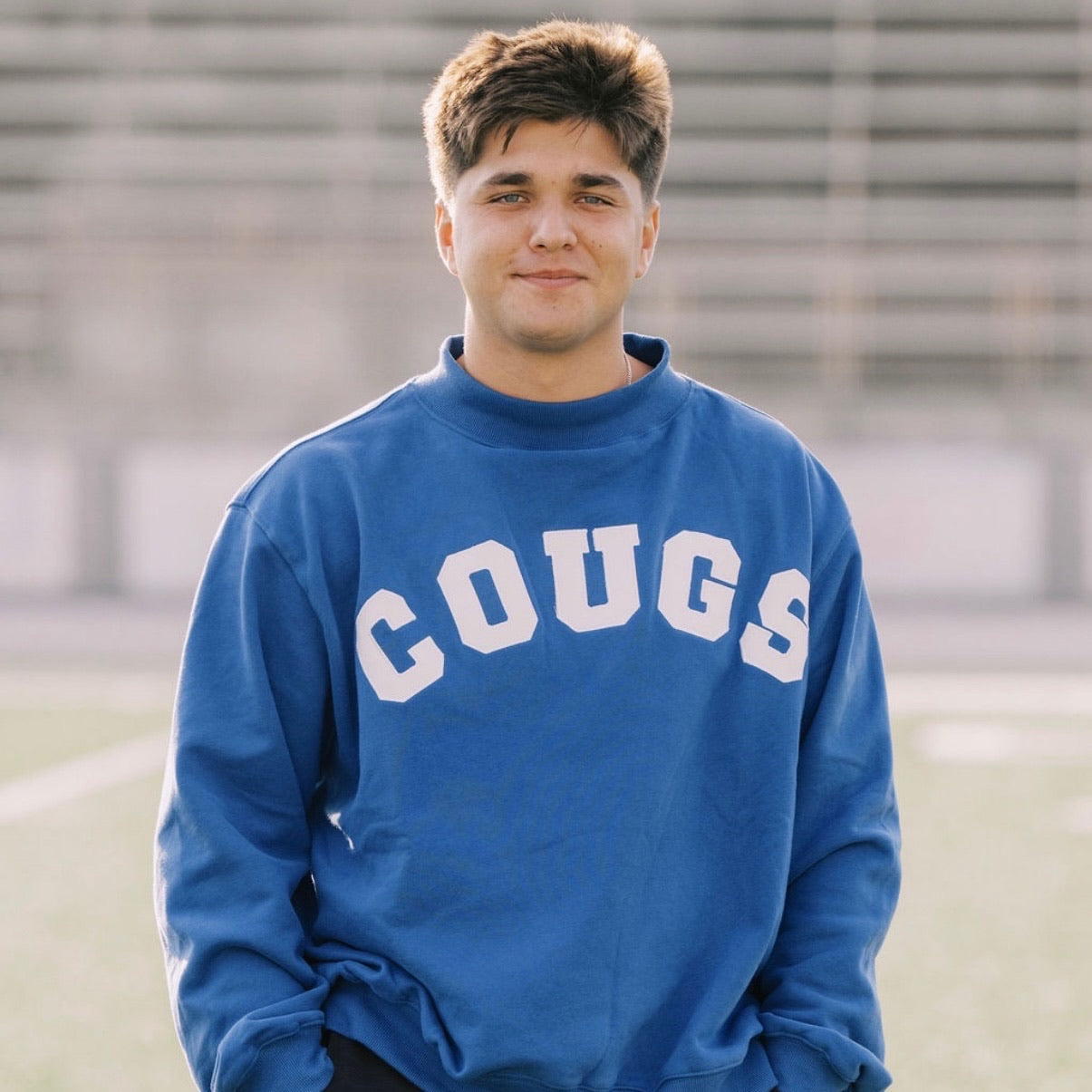Person wearing a blue sweatshirt with 'COUGS' printed on it, standing outdoors.