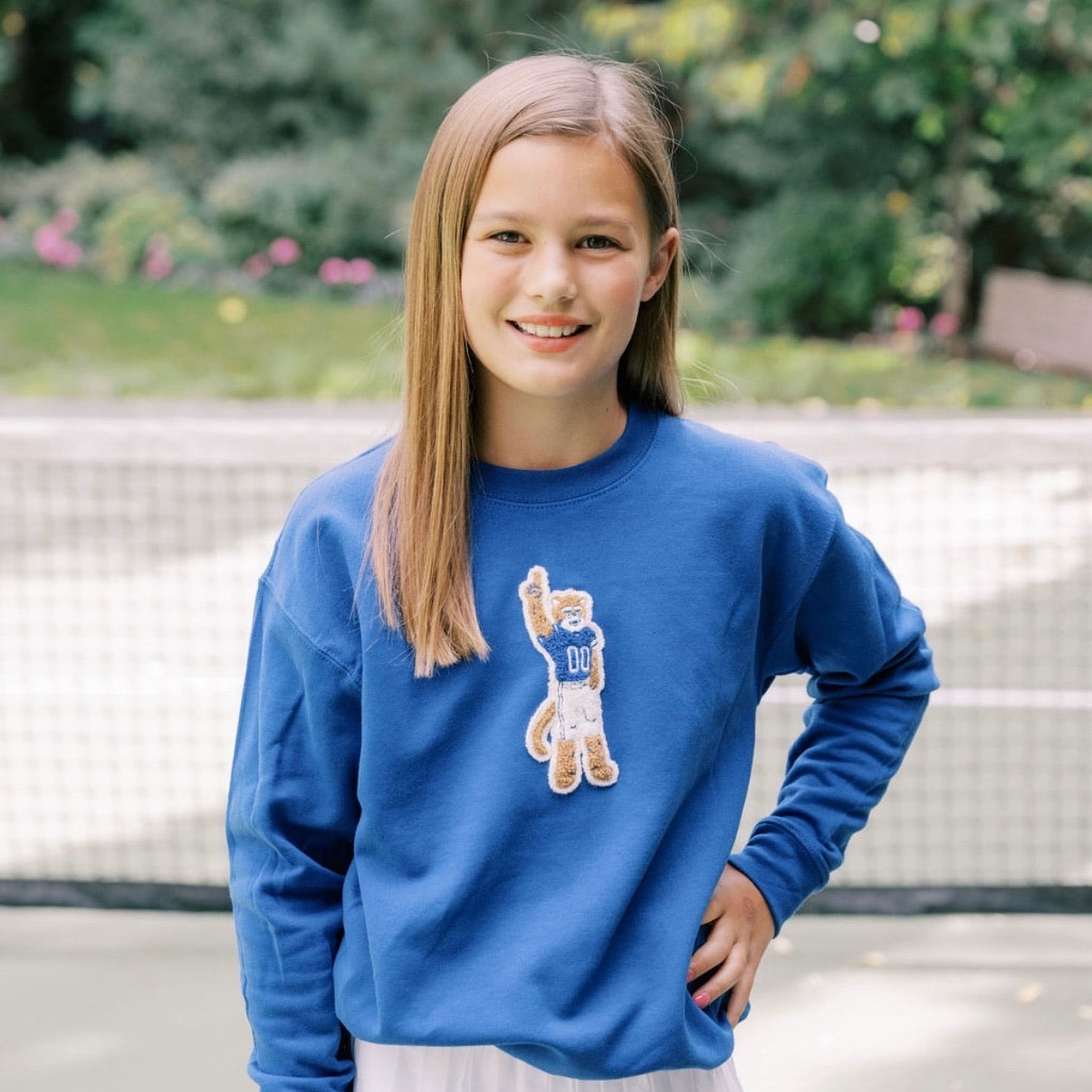 Young girl wearing a blue sweatshirt with a bear graphic outdoors